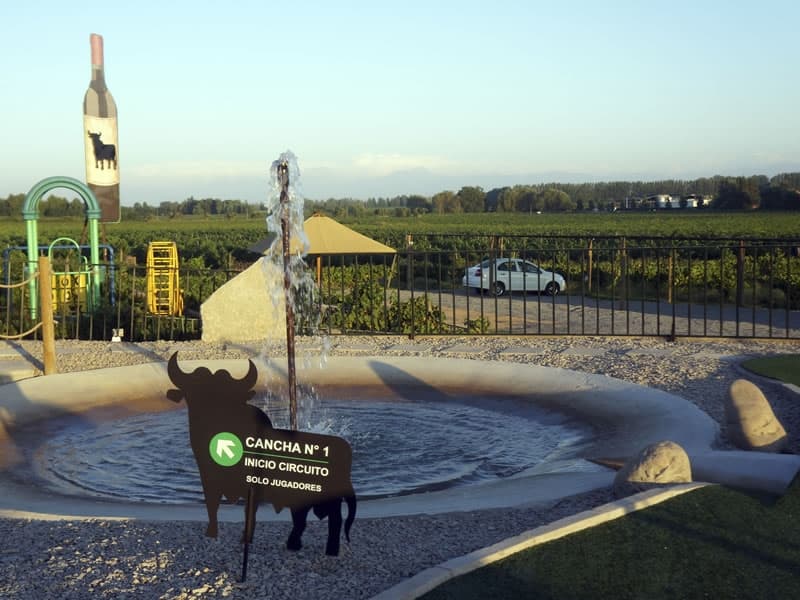 Fuente de la cancha 1 del mini golf, con los juegos infantiles y el viñedo detrás